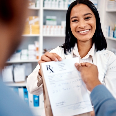 A pharmacist smiling while taking a prescription from a customer