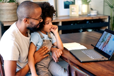 A parent with their child in their lap both speaking to a Doctor through a video chat on their laptop