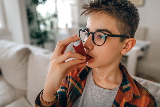 A tweenage boy uses his inhaler.