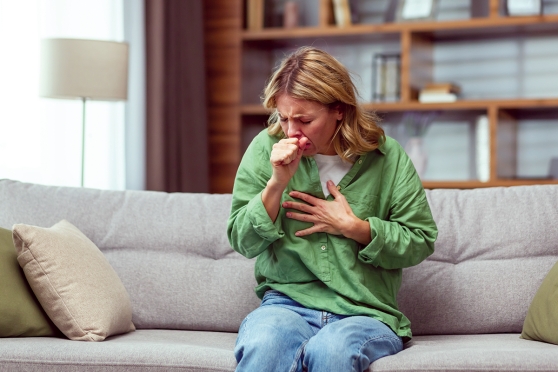 A woman in a green blouse is coughing and holding her chest.